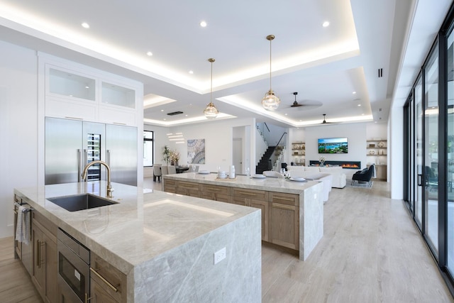 kitchen with ceiling fan, sink, built in appliances, pendant lighting, and a tray ceiling