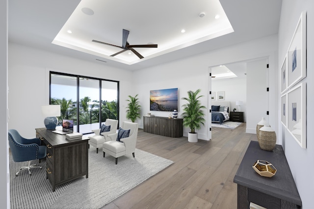 living room featuring a tray ceiling, ceiling fan, and light wood-type flooring