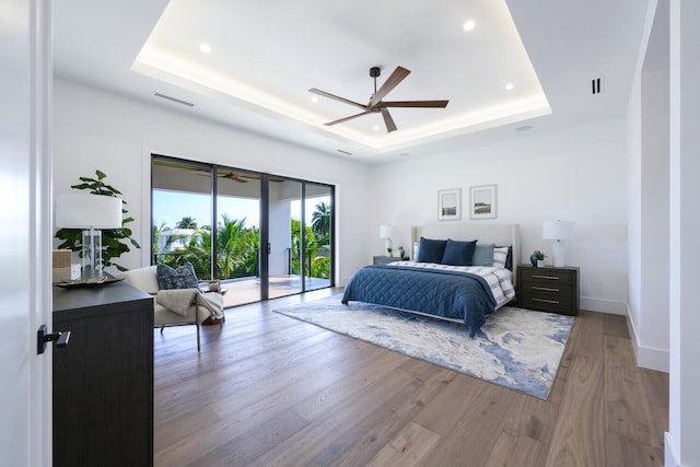 bedroom featuring a tray ceiling, ceiling fan, hardwood / wood-style floors, and access to outside