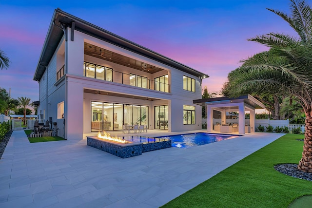 back house at dusk featuring ceiling fan, a fire pit, a balcony, a swimming pool with hot tub, and a patio