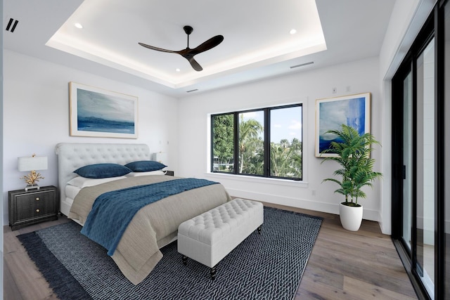 bedroom with hardwood / wood-style floors, ceiling fan, and a tray ceiling