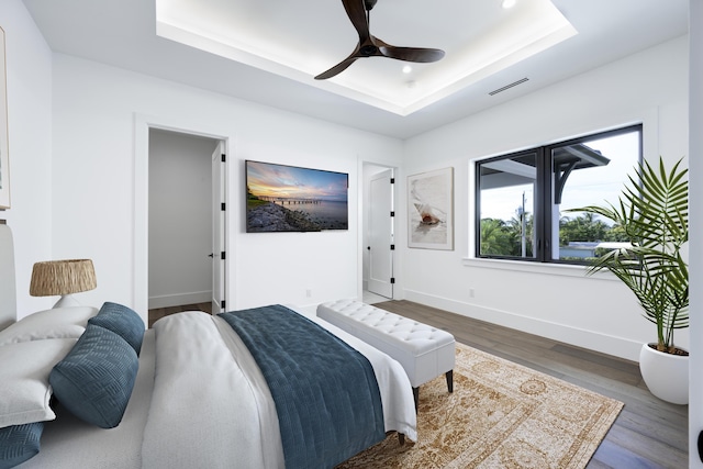 bedroom with ceiling fan, wood-type flooring, and a tray ceiling