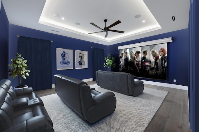 home theater room with hardwood / wood-style floors, ceiling fan, and a raised ceiling