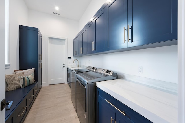 laundry room with washer and clothes dryer, cabinets, sink, and light hardwood / wood-style flooring