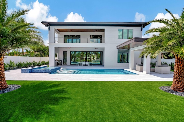 rear view of property with a balcony, ceiling fan, a swimming pool with hot tub, a patio area, and a yard