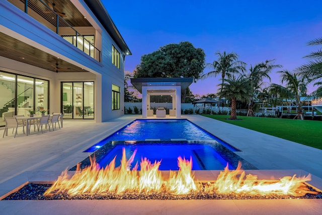 pool at dusk featuring an in ground hot tub, an outdoor fire pit, a patio area, and ceiling fan