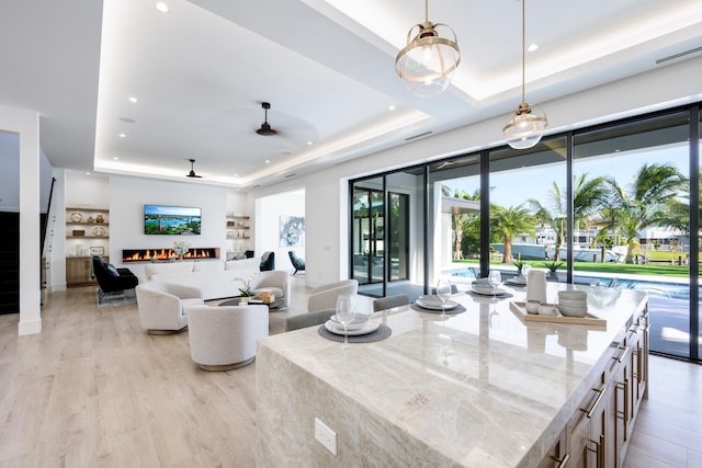 living room featuring a fireplace, light wood-type flooring, a tray ceiling, and ceiling fan