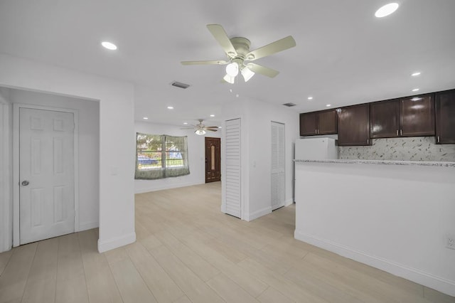 kitchen with light stone countertops, dark brown cabinetry, white refrigerator, and ceiling fan