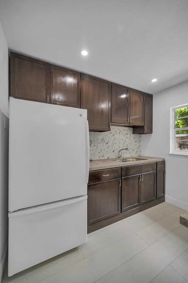 kitchen with decorative backsplash, sink, white fridge, and dark brown cabinets