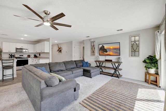 living room with carpet, ceiling fan, and a textured ceiling