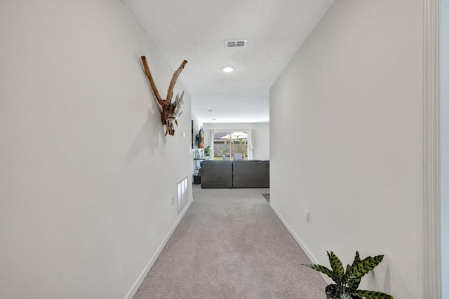 hallway featuring baseboards, carpet flooring, a textured ceiling, and visible vents