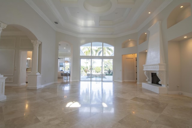 unfurnished living room with ornamental molding, a fireplace, a high ceiling, and decorative columns