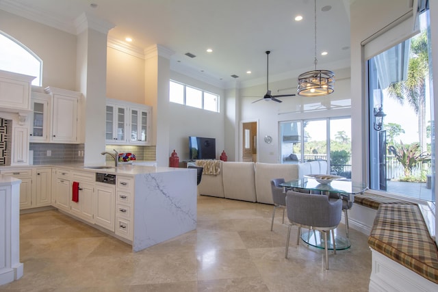 kitchen featuring tasteful backsplash, light stone counters, ceiling fan with notable chandelier, white cabinets, and hanging light fixtures