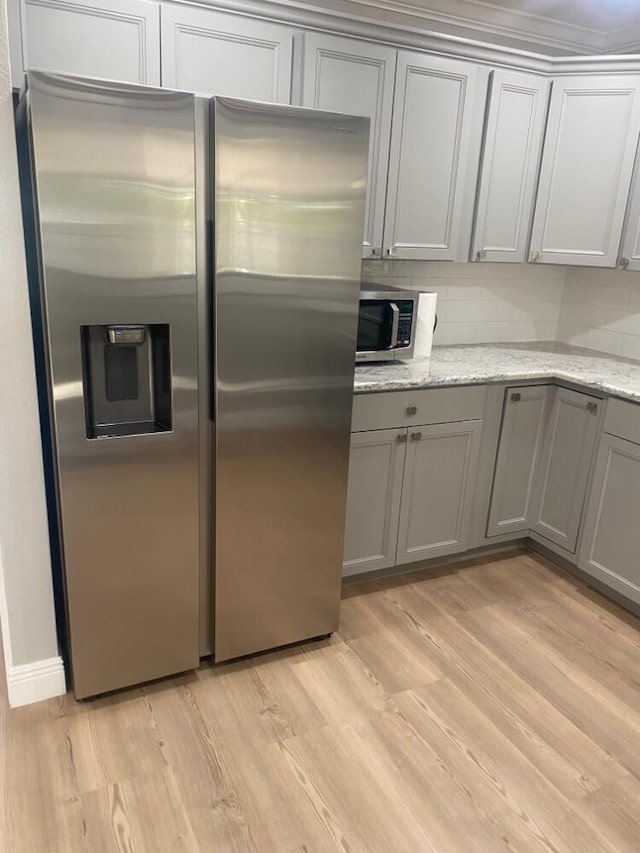 kitchen with stainless steel appliances, light hardwood / wood-style floors, gray cabinetry, and light stone countertops