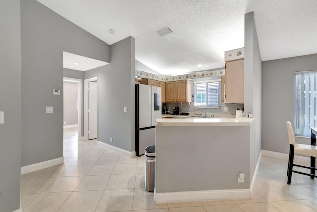 kitchen with a textured ceiling, light brown cabinets, light tile patterned floors, white fridge, and lofted ceiling