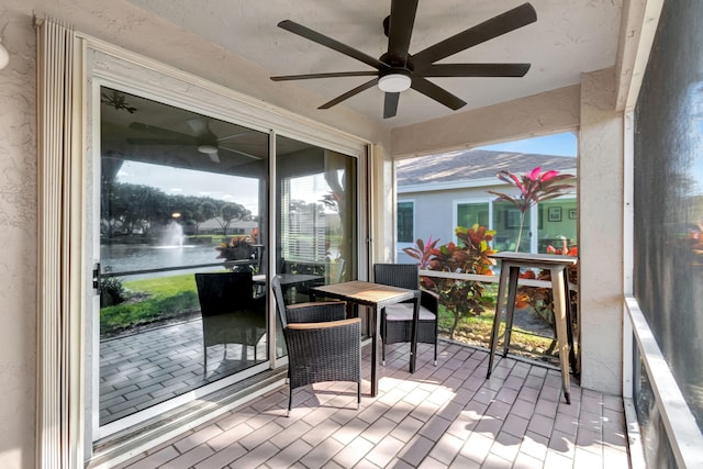 sunroom with ceiling fan and a water view