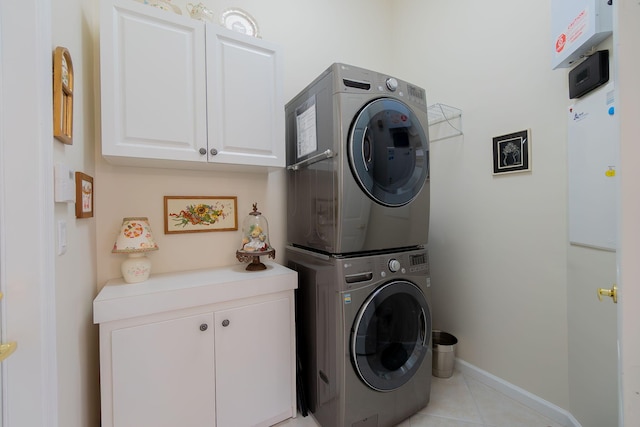 laundry room featuring light tile patterned floors, cabinets, and stacked washer and clothes dryer