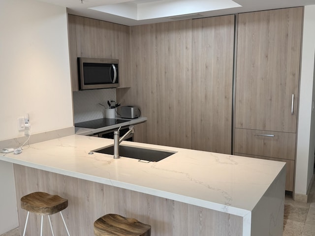 kitchen with kitchen peninsula, a breakfast bar, light stone countertops, and sink