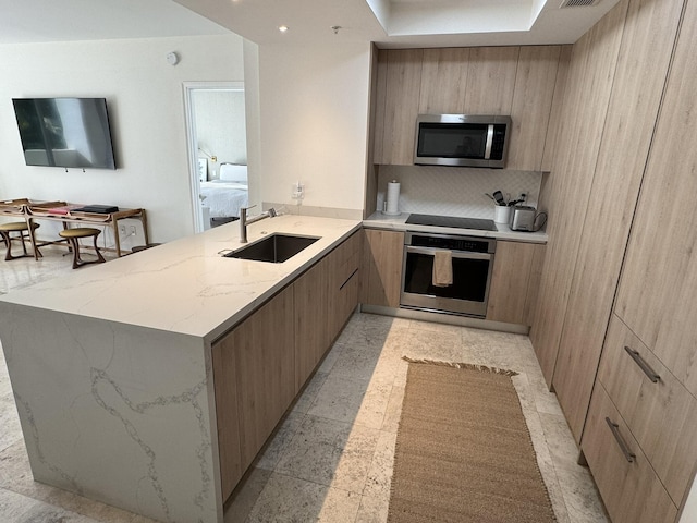 kitchen featuring light stone countertops, sink, stainless steel appliances, kitchen peninsula, and decorative backsplash