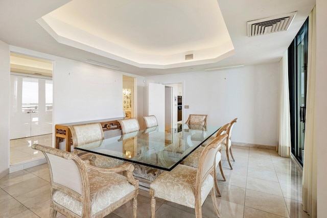 dining area with light tile patterned floors, a raised ceiling, visible vents, and baseboards