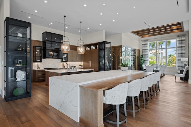 kitchen featuring pendant lighting, a center island with sink, a kitchen breakfast bar, light stone countertops, and tasteful backsplash