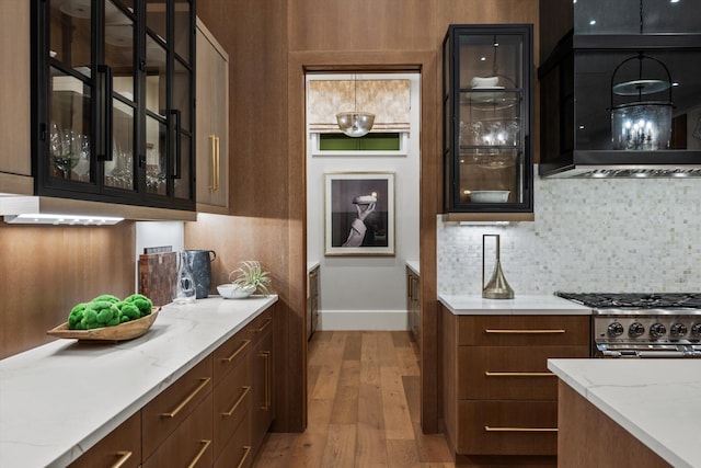 bar featuring light stone counters, ventilation hood, decorative backsplash, dark brown cabinets, and light wood-type flooring