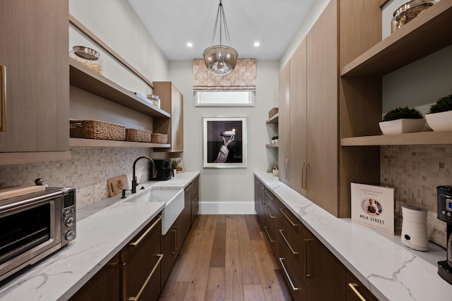 interior space featuring light wood-type flooring, tasteful backsplash, light stone counters, sink, and hanging light fixtures