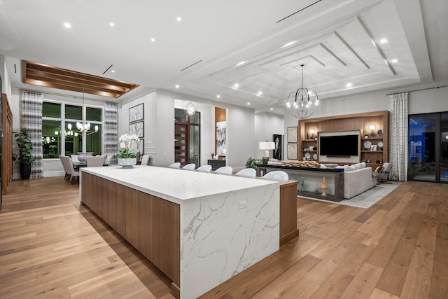 kitchen with light stone countertops, an inviting chandelier, a spacious island, a tray ceiling, and light wood-type flooring