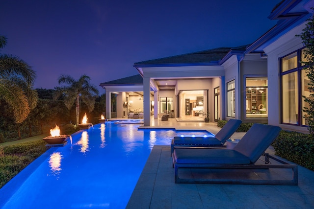 pool at night with an in ground hot tub, a patio, and an outdoor fire pit