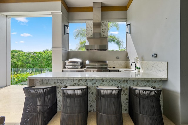 kitchen featuring kitchen peninsula, a kitchen bar, sink, wall chimney range hood, and range