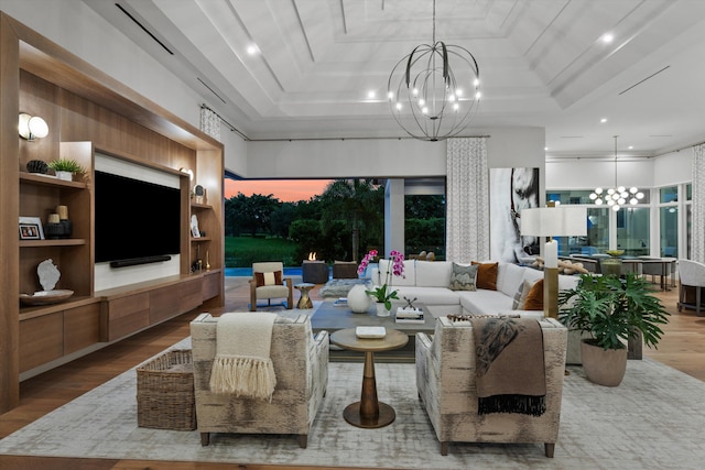 living room with a tray ceiling, light hardwood / wood-style flooring, built in features, and a notable chandelier