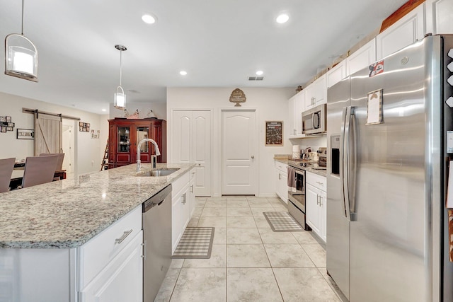 kitchen featuring appliances with stainless steel finishes, white cabinets, pendant lighting, a barn door, and a kitchen island with sink