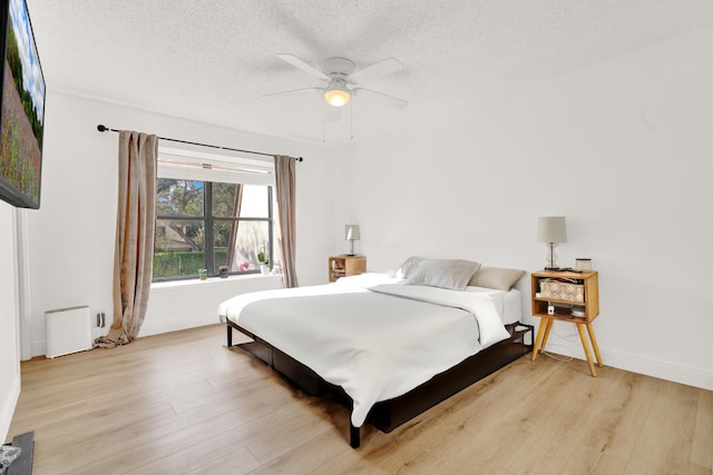 bedroom with ceiling fan, light hardwood / wood-style floors, and a textured ceiling