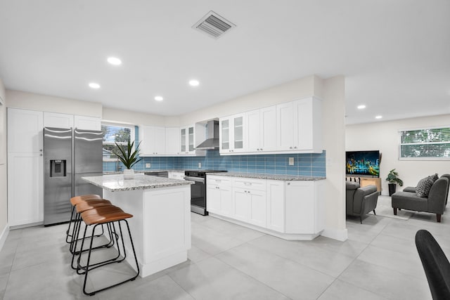 kitchen with light stone countertops, appliances with stainless steel finishes, white cabinetry, and wall chimney exhaust hood