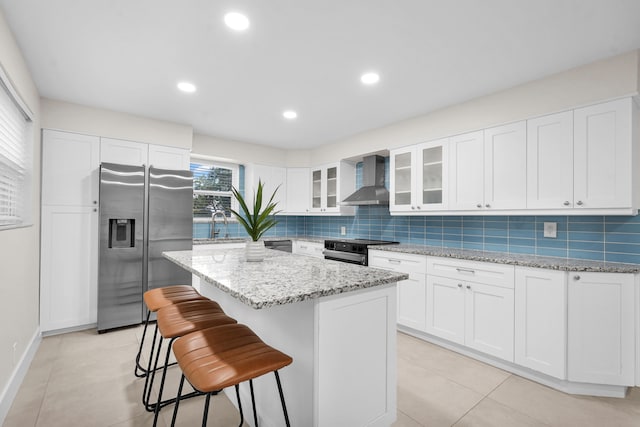 kitchen with a center island, white cabinetry, wall chimney range hood, and stainless steel appliances