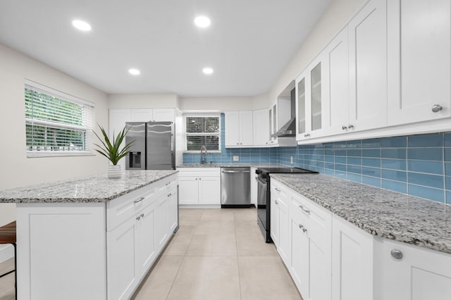 kitchen featuring appliances with stainless steel finishes, backsplash, light stone counters, white cabinets, and a kitchen island