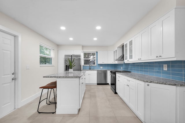 kitchen featuring a breakfast bar, a kitchen island, light stone counters, white cabinetry, and stainless steel appliances