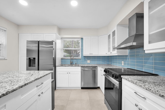 kitchen with appliances with stainless steel finishes, sink, white cabinetry, and wall chimney range hood