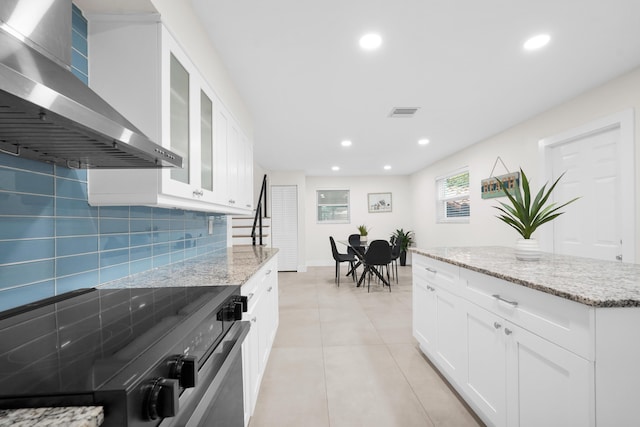 kitchen with white cabinets, light stone counters, wall chimney exhaust hood, and stainless steel electric range