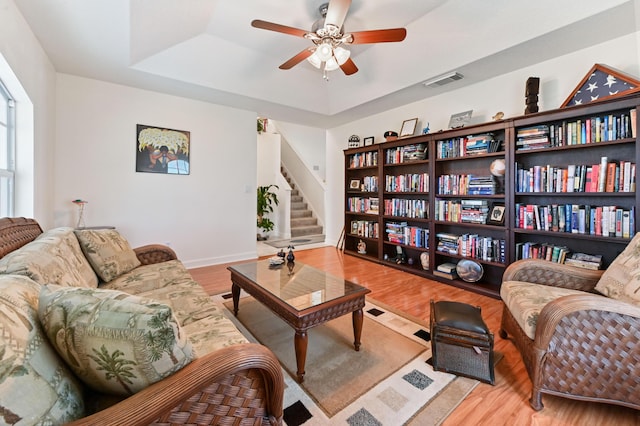 living room with hardwood / wood-style floors, a tray ceiling, and ceiling fan