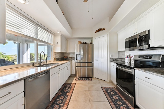 kitchen featuring backsplash, sink, appliances with stainless steel finishes, light tile patterned flooring, and white cabinetry