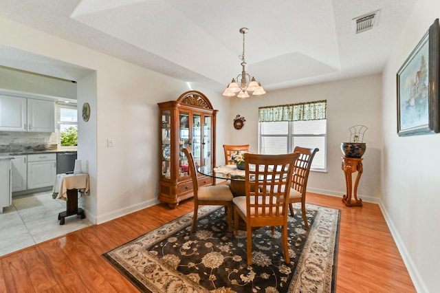 dining space with a chandelier, a tray ceiling, and light hardwood / wood-style flooring