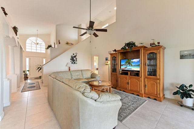 living room featuring ceiling fan with notable chandelier, light tile patterned floors, a towering ceiling, and decorative columns