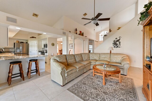 tiled living room featuring ceiling fan with notable chandelier, high vaulted ceiling, and decorative columns