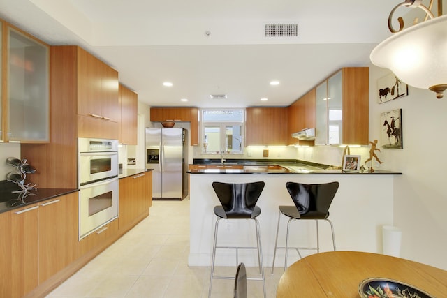 kitchen featuring a breakfast bar, a wealth of natural light, stainless steel refrigerator with ice dispenser, and multiple ovens