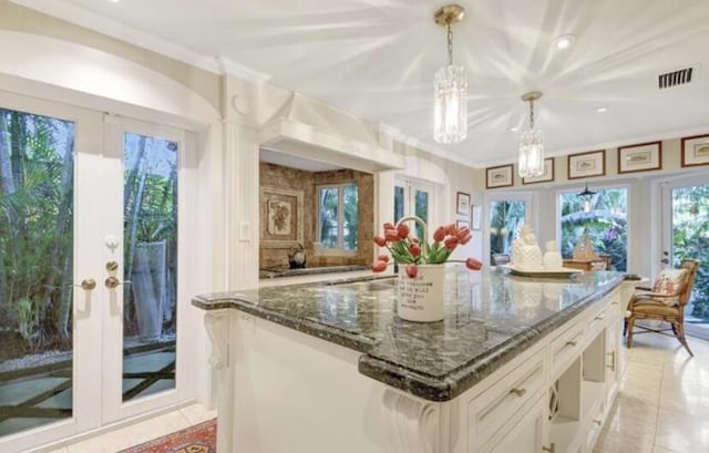 kitchen with white cabinetry, an island with sink, dark stone counters, decorative light fixtures, and light tile patterned floors