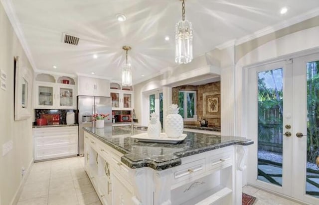 kitchen featuring french doors, stainless steel refrigerator with ice dispenser, dark stone countertops, pendant lighting, and a spacious island