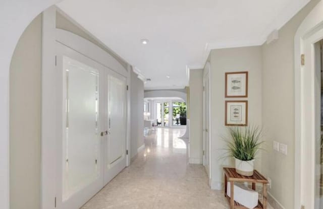 hall with french doors, ornamental molding, and light tile patterned flooring