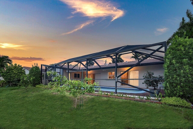 back house at dusk featuring a lanai and a yard