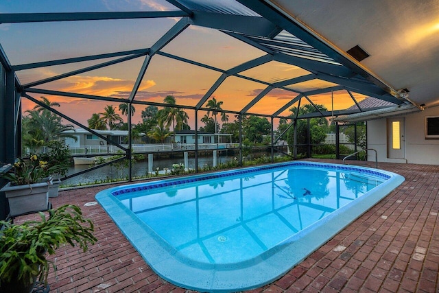 pool at dusk featuring a lanai, a water view, and a patio